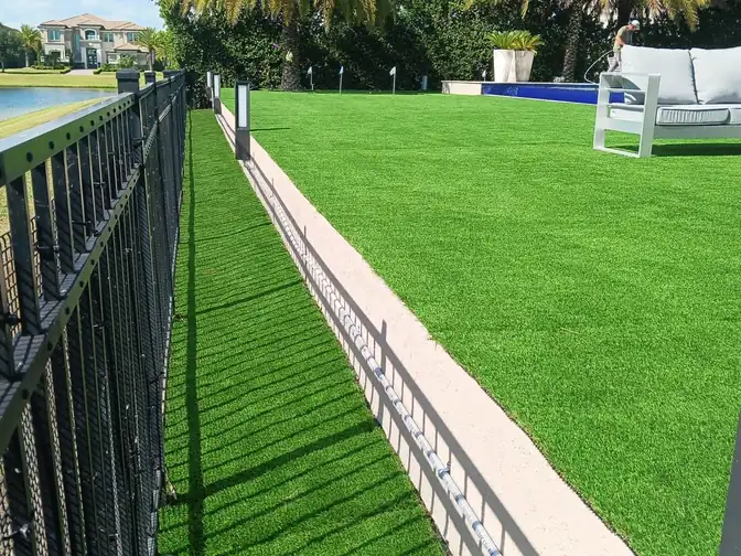 Large lakefront yard covered in artificial turf, running from an aluminum picket fence past path lights to a pool, an outdoor sofa and putting green flags