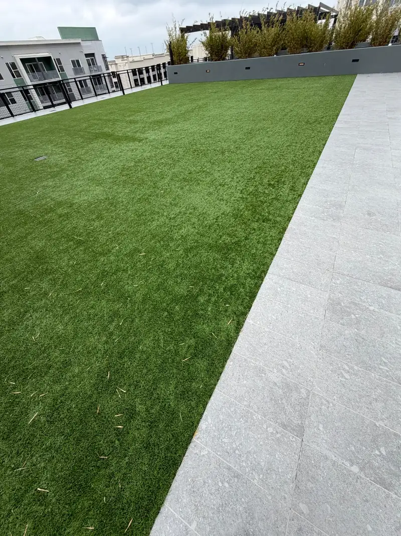 Rooftop amenity deck with artificial turf laid beside large-format porcelain pavers, bamboo planters and a pergola