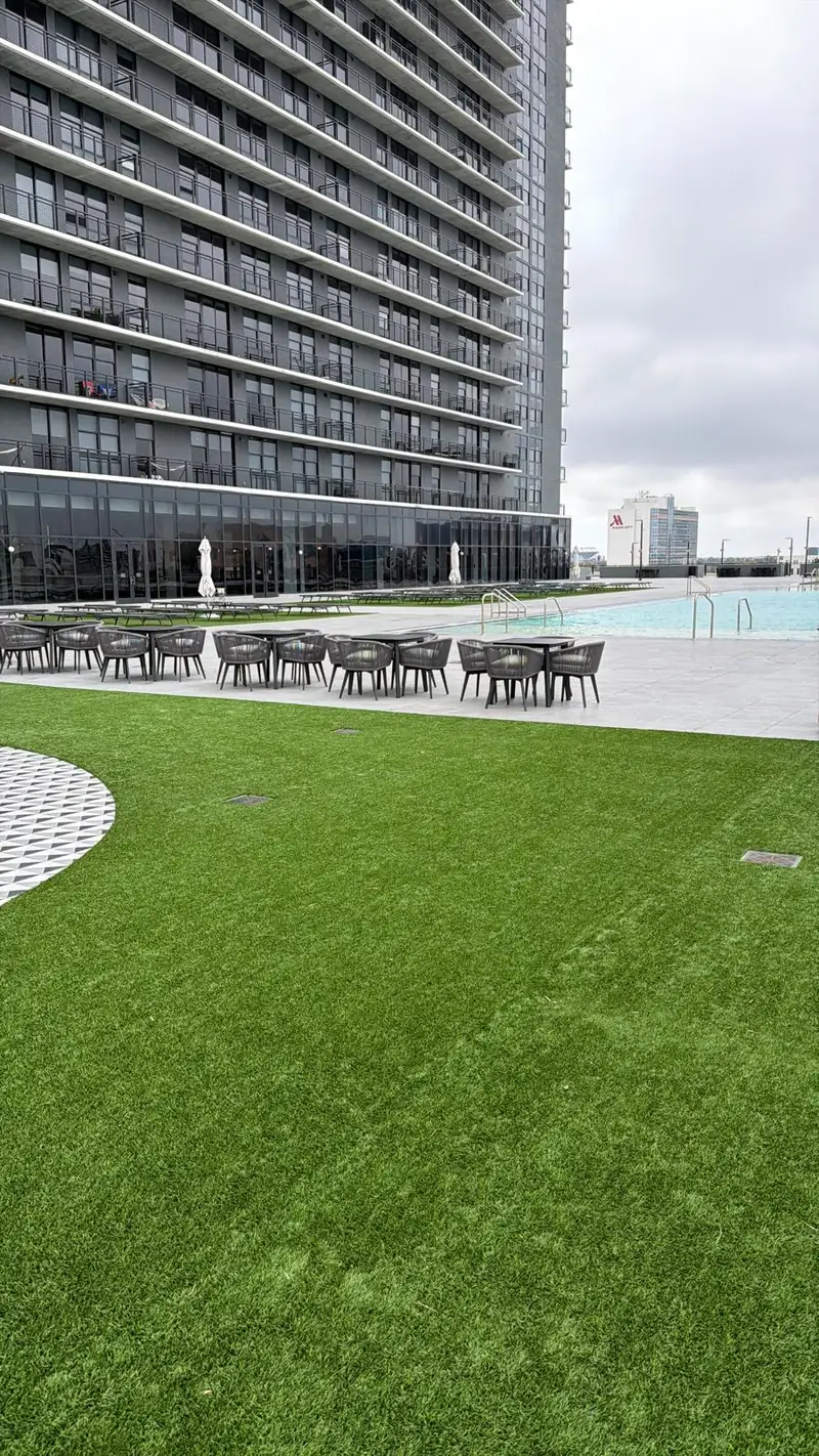 Artificial turf lawn on a high-rise rooftop pool deck with lounge chairs, cafe tables and drain grates set flush in the turf