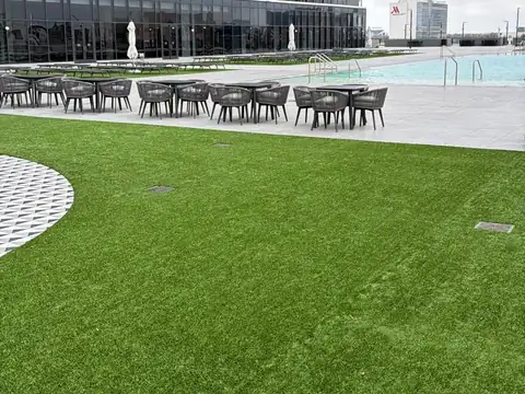 Artificial turf lawn on a high-rise rooftop pool deck with lounge chairs, cafe tables and drain grates set flush in the turf